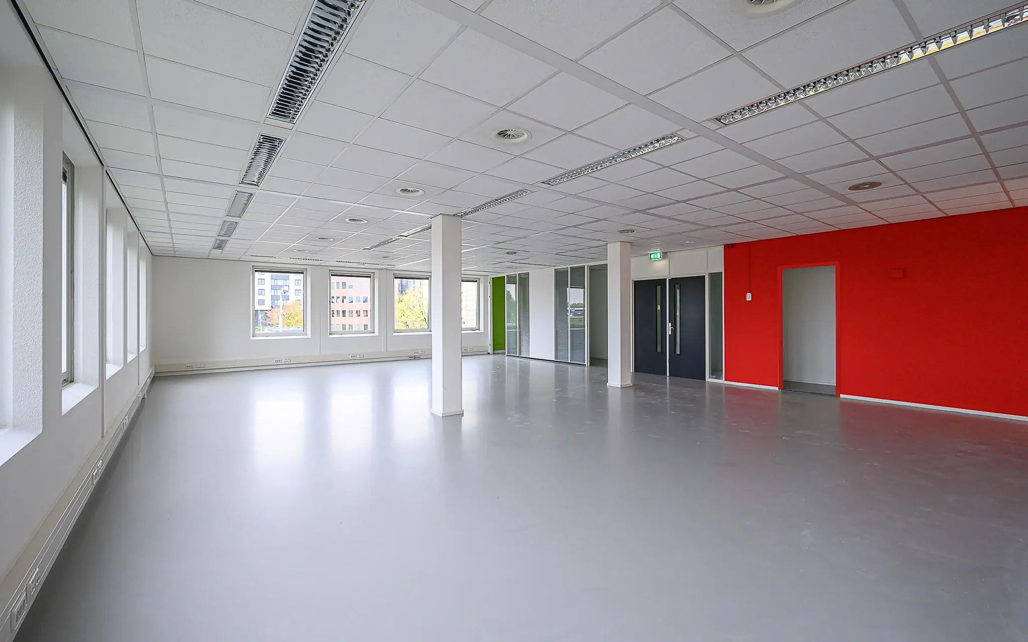 Leeg en modern kantoorpand aan de Rivium Westlaan met grijze vloer, systeemplafond en rode accentmuur.